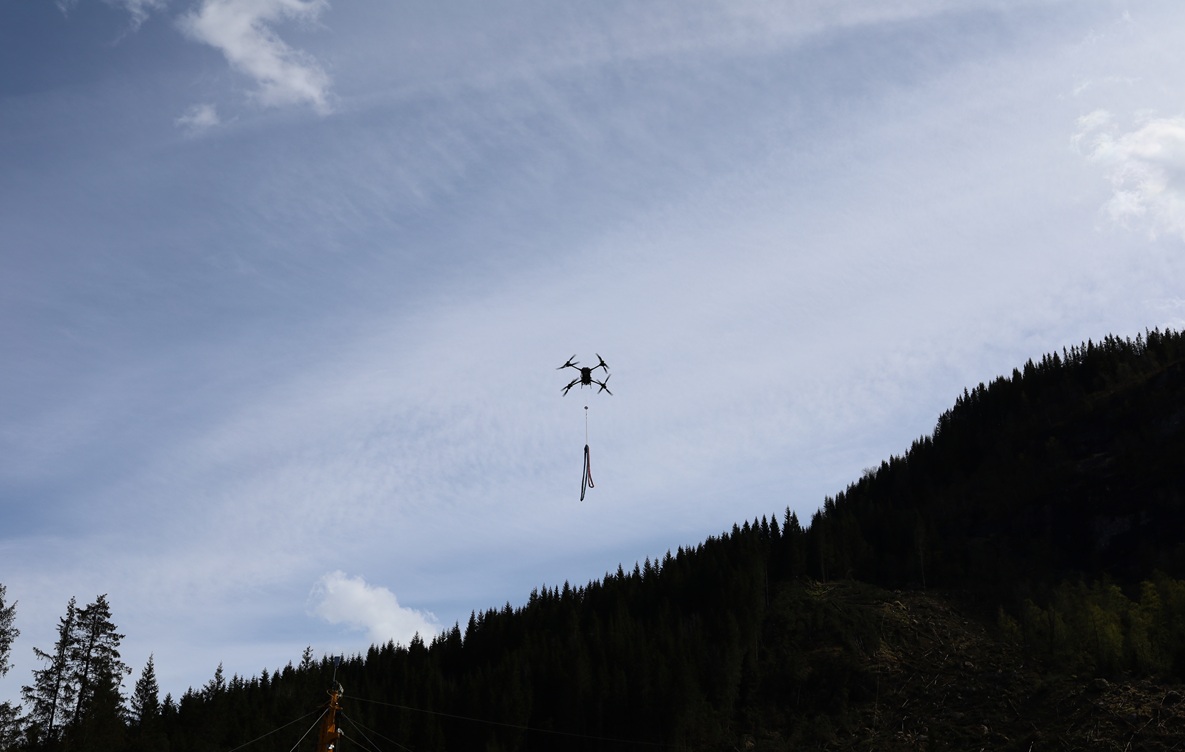 Drone med lastekrok over skogsterreng